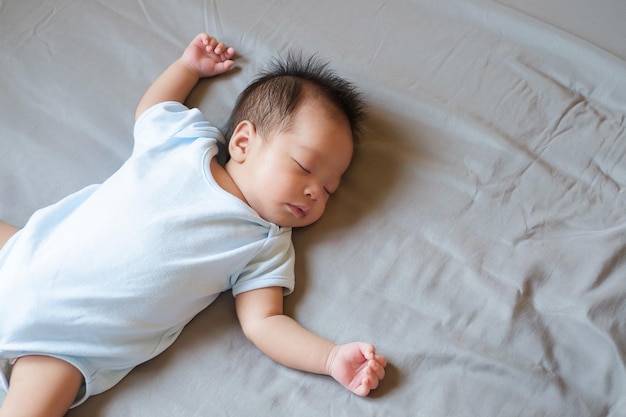 Asiatisches Baby schläft auf grauem Bett