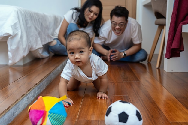 Asiatisches Babykriechen und Spielen des Balls auf dem Bretterboden