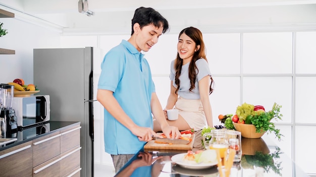 Asiatisches fröhliches Liebespaar, das sich mit Freude beim Zubereiten und Kochen unterhält, während es zu Hause auf einer Küchentheke steht Gemeinsam in ihren Küchen zu Hause kochen