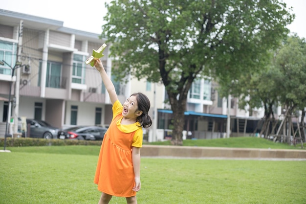 Asiatisches glückliches Mädchen mit orangefarbenem Kleid spielt auf dem Spielplatz