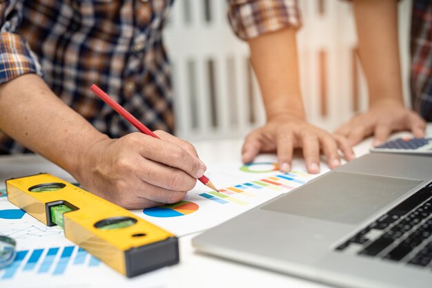 Foto asiatisches ingenieur- und partnerteam lernt und spricht mit hausplan-projekt-blueprint-graphik und gelbem helm und ingenieurkonstruktionswerkzeugen auf der tischarbeit