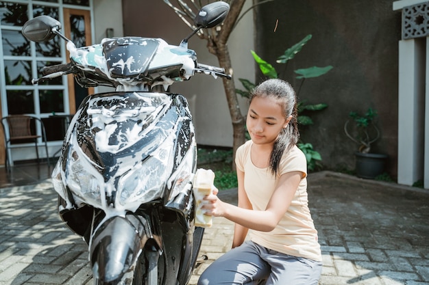 Asiatisches junges Mädchen, das ein Motorrad wäscht