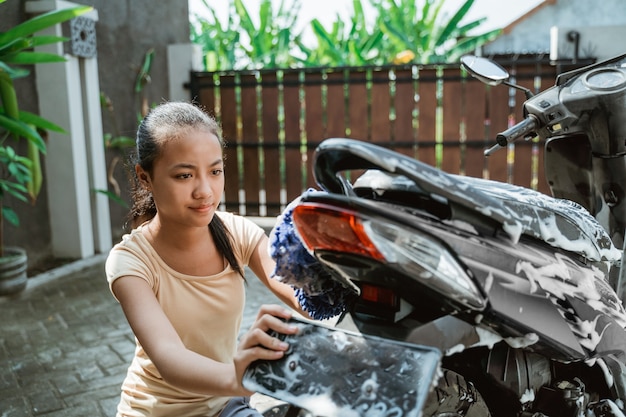 Asiatisches junges Mädchen, das ein Motorrad wäscht