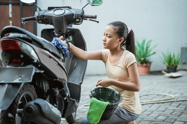 Asiatisches junges Mädchen, das ein Motorrad wäscht