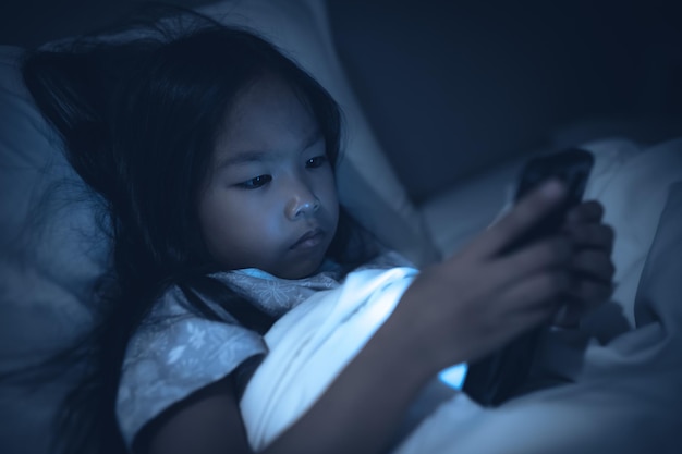 Asiatisches Kind, das nachts auf dem Smartphone im Bett spieltDas Mädchen Addict Social Media