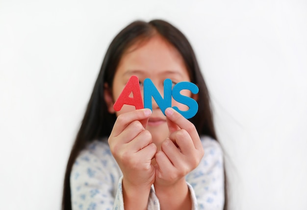 Foto asiatisches kind des kleinen mädchens, das ans-schwammtext in den händen über weißem hintergrund hält. bildungs- und entwicklungskonzept. fokus auf buchstaben in der hand