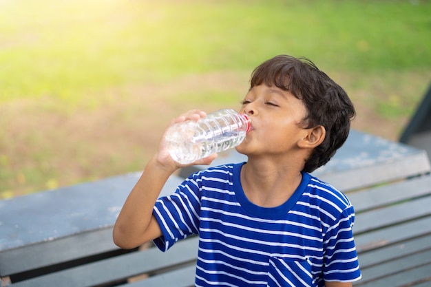 Asiatisches Kind durstiges Wasser und Trinkwasser von einer transparenten Plastikflasche im Park.