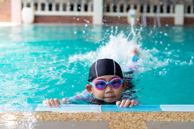 Asiatisches Kind kleines Mädchen mit Badeanzug und Mütze mit Brille am Rand des Schwimmbeckens Lernen Sie, Ideenkonzept zu schwimmen