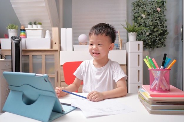 Asiatisches Kind verwendet Tablet-Tablet, um seine Online-Lektion zu Hause zu lernen