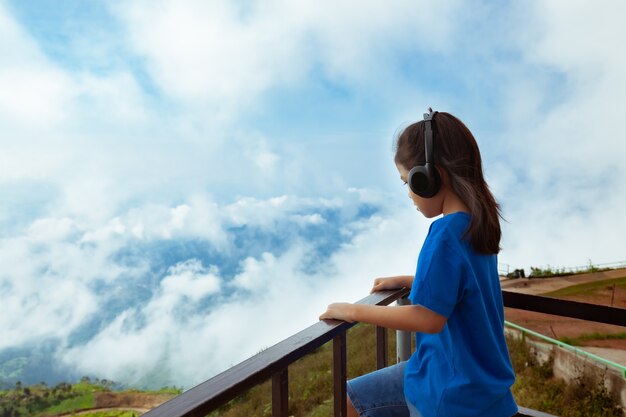 Asiatisches Kindermädchen, das die Musik mit Kopfhörer hört und den schönen Nebel und Berg mit Frische und Glück betrachtet