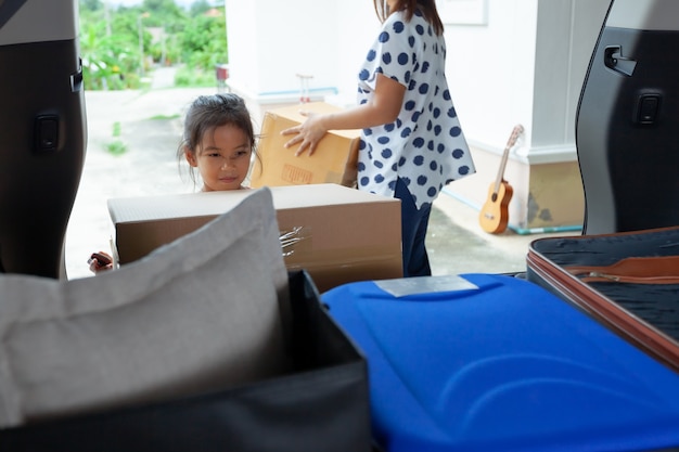 Asiatisches Kindermädchen, das Eltern hilft, einen Karton mit Sachen zu tragen, die in das Auto bewegen