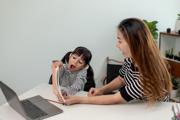 Asiatisches kleines junges Mädchen, das zu Hause Online-Unterricht mit Mutter lernt