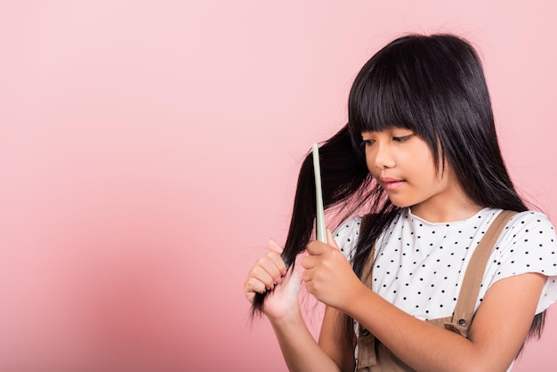 Asiatisches kleines Kind, 10 Jahre alt, hält Kamm, der sie widerspenstig bürstet, berührt sie ihr langes schwarzes Haar