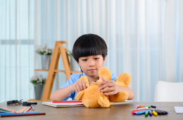 Asiatisches kleines Kind allein zu Hause und spielt mit Puppe. Sohn mit Spielzeug als Freund. Einsamer Junge unglücklich.