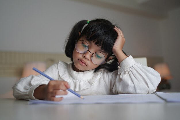 Asiatisches kleines Kindermädchen, das Brillen trägt, macht eine Hausarbeit zu Hause.