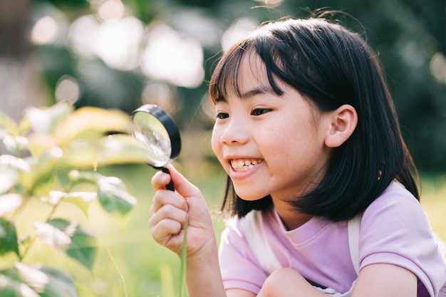 Asiatisches kleines Mädchen benutzt Lupe, um im Park zu spielen