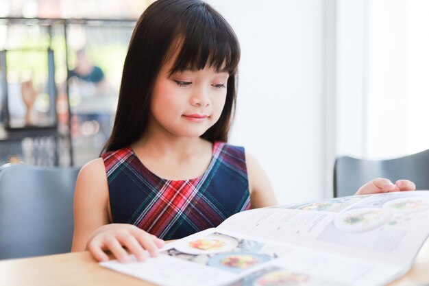 Asiatisches kleines Mädchen, das Buchlächeln und glückliches Gesicht liest