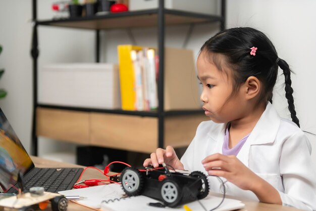 Asiatisches kleines Mädchen, das im MINT-Kurs einen Roboter konstruiert und programmiert. Mechaniker-Spielzeugauto reparieren und reparieren