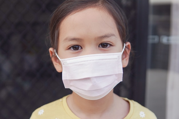 Asiatisches kleines Mädchen, das medizinische Gesichtsmaske, Selbstquarantäne, Coronavirus, Epidemiepandemie des Ausbruchs des Covid-19-Virus trägt