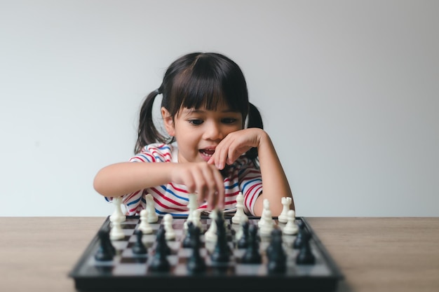 Asiatisches kleines Mädchen, das Schach zu Hause spielt, eine Partie Schach