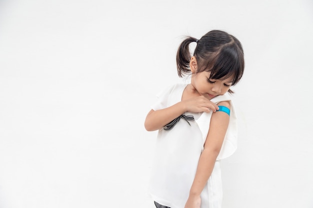 Asiatisches kleines Mädchen, das seinen Arm zeigt, nachdem es geimpft oder geimpft wurde
