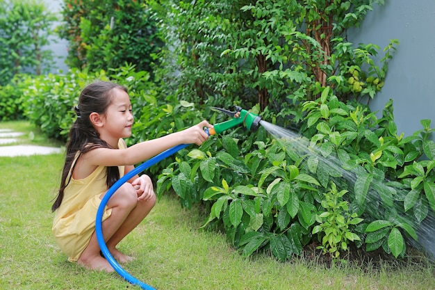 Asiatisches kleines Mädchen, das Wasserspray auf Bäume gießt