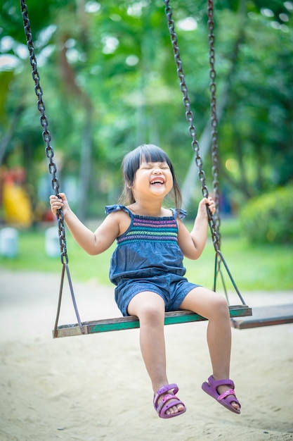 Asiatisches kleines Mädchen genießt, ein Schwingen in einem Kinderspielplatz zu spielen