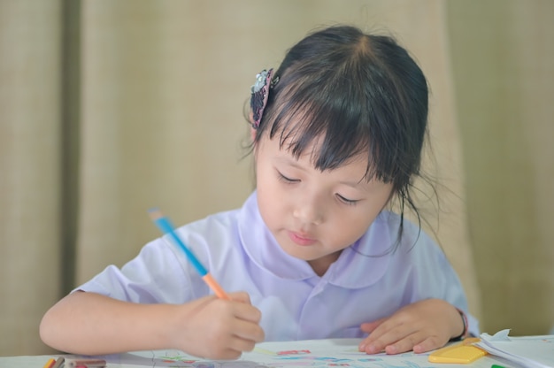 Asiatisches kleines Mädchen in der Vorschuluniform, die Schulhausaufgaben zeichnet und malt