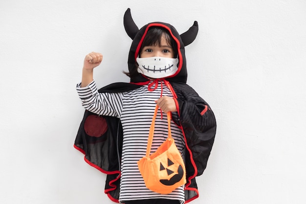 Asiatisches kleines Mädchen in einem Halloween-Kostüm in einer medizinischen Maske. Halloween mit Sicherheitsmaßnahmen von Covid-19