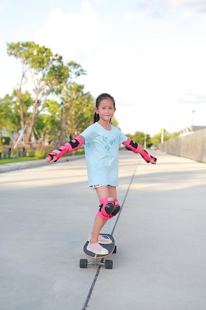 Asiatisches kleines Mädchen mit Sicherheits- und Schutzausrüstung beim Skaten auf einem Skateboard. Kind reitet auf Skateboard im Freien auf der Straße