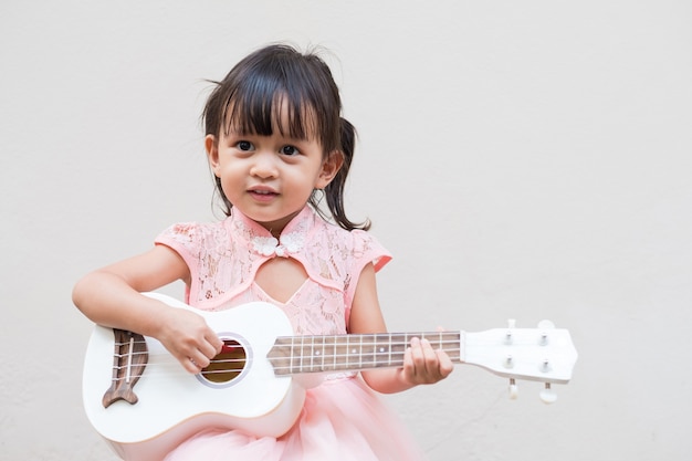 Asiatisches kleines Mädchen spielt Ukulele mit vollem Glücksmoment