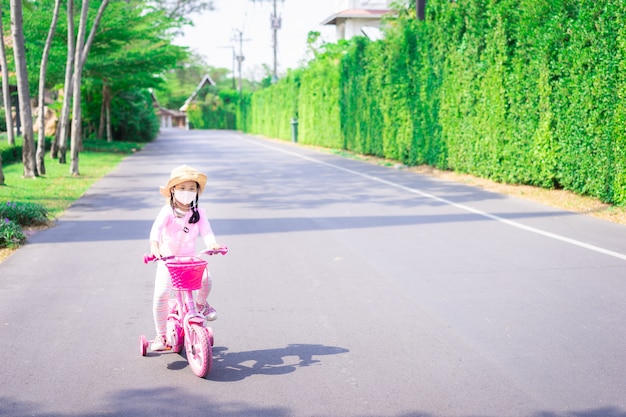 Asiatisches kleines Mädchen tragen eine Maske gegen PM 2.5 Luftverschmutzung oder Krankheit, während Sie Fahrrad fahren