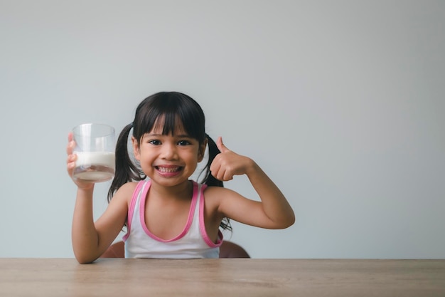 Asiatisches kleines Mädchen trinkt Milch aus einem Glas, das sie sehr glücklich war