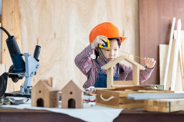 Asiatisches kleines Mädchen Zimmermann arbeitet an Holzbearbeitung in der Tischlerei Zimmermann arbeitet an Holzhandwerk in der Werkstatt Baumaterial Holzmöbel Asiatisches kleines Mädchen arbeitet in einer Tischlerei