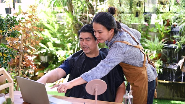 Asiatisches Liebespaar, das Haarschnitt macht, um sein Aussehen zu Hause aufzufrischen. Salon und Friseursalon im Garten.