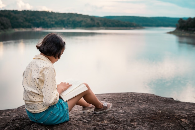 Asiatisches Mädchen, das ein Buch durch den See liest