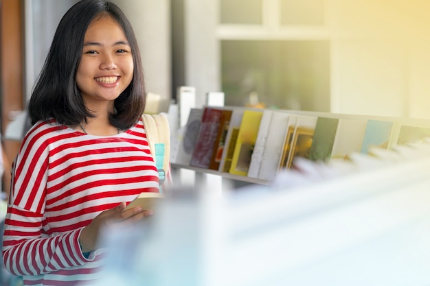 Asiatisches Mädchen, das ein Buch in den Buchhandlungen stehend und lächelnd liest