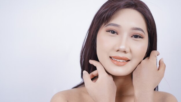 Asiatisches Mädchen, das ihr Gesicht mit Make-up lokalisiert auf weißem Hintergrund zeigt