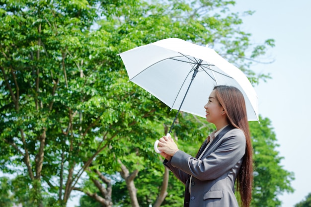 Asiatisches Mädchen, das im Büro arbeitet Sie hielt einen Sonnenschirm im heißen Wetter.