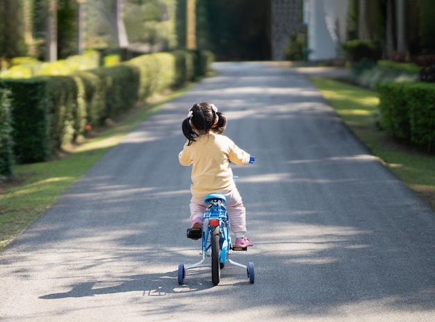 Asiatisches Mädchen, das lernt, im Parkgarten Fahrrad zu fahren Bildungskonzept für Kinder, die Radfahren im Park Baby Sportkonzept üben