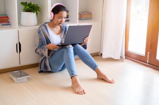 Asiatisches Mädchen, das mit Laptop und Kopfhörern im Wohnzimmer sitzt, lernt zu Hause