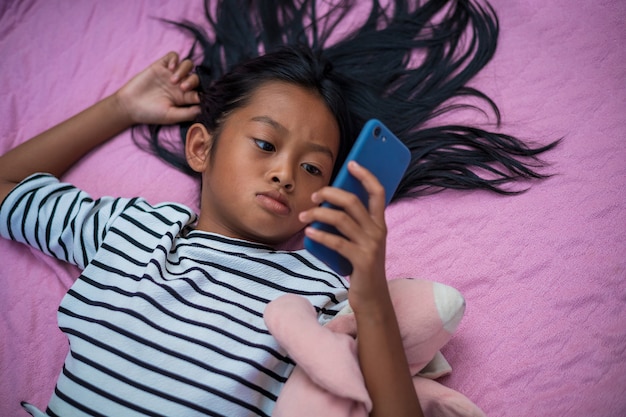 Asiatisches Mädchen, das morgens mit einem Smartphone Inhalte auf ihrem Bett anschaut