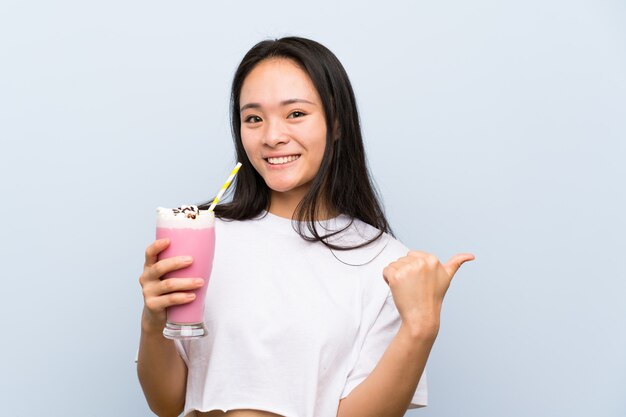 Asiatisches Mädchen des Jugendlichen, das ein Erdbeermilchshake zeigt auf die Seite hält, um ein Produkt darzustellen