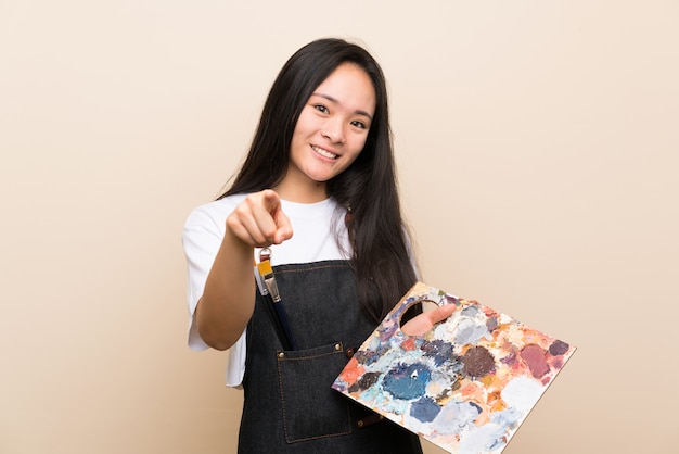 Asiatisches Mädchen des Jugendlichmalers zeigt Finger auf Sie mit einem überzeugten Ausdruck