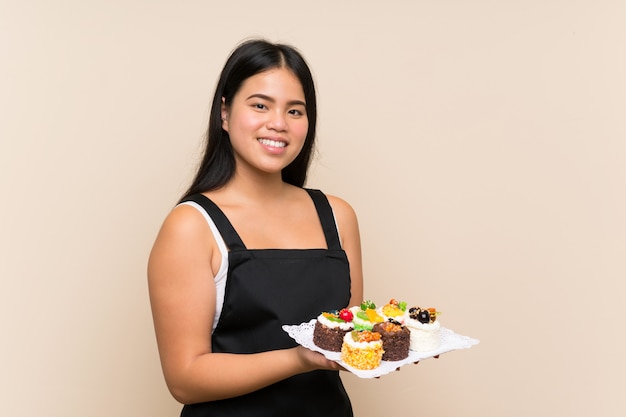 Asiatisches Mädchen des jungen Jugendlichen, das viele verschiedene Minikuchen über lokalisierter Wand hält