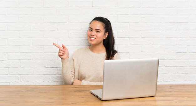 Asiatisches Mädchen des jungen Jugendlichen mit einem Laptop in einer Tabelle Finger auf die Seite zeigend