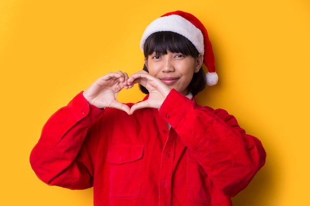 Asiatisches Mädchen gekleidet in Weihnachtsmütze mit einer Weihnachtsliebesgeste