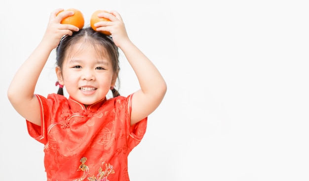 asiatisches Mädchen im chinesischen Trachtenkleid, das Mandarine lächelt und hält.