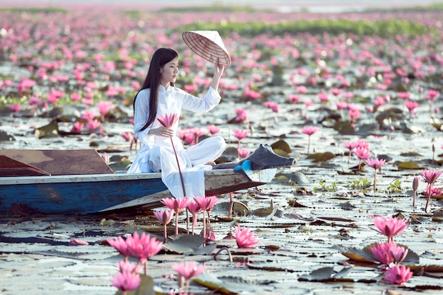 Asiatisches mädchen im nationalen kostüm von vietnam sitzend auf dem boot im meer des roten lotos in undon thani, thailand.