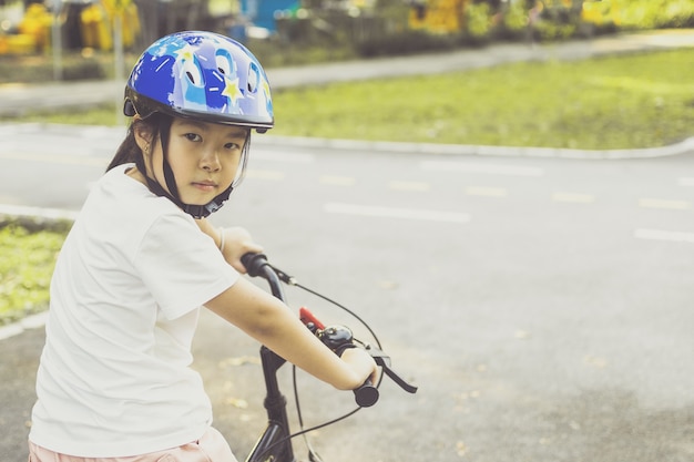 Asiatisches Mädchen lernt im Park Fahrrad zu fahren. Porträt eines netten Kindes auf dem Fahrrad.